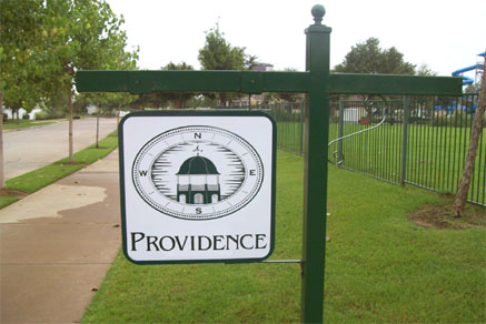 Square sign with rounded corners advertising the Providence development while hanging from a green steel post