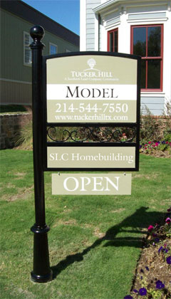 A green sign attached to a single black post identifying a model home at the Tucker Hill development