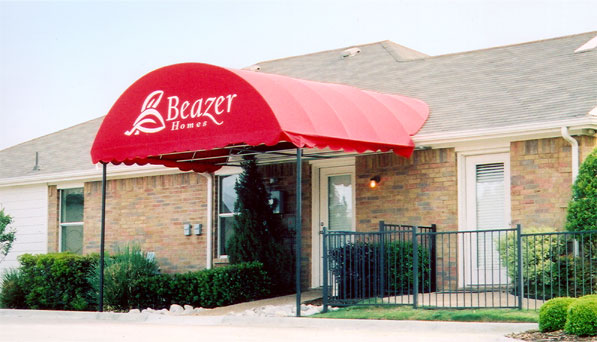 A red awning with an arched top mounted over the front door of a model home