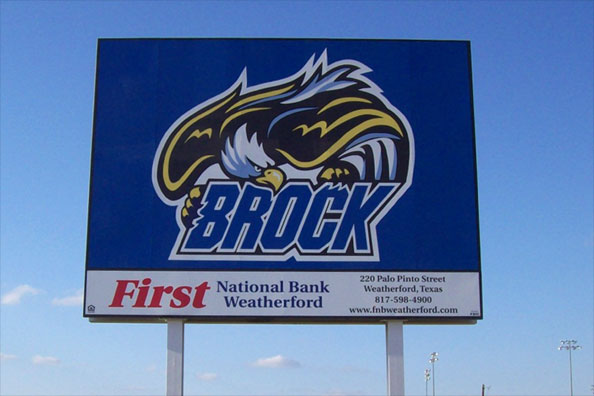 A large billboard at a sports stadium displaying the school's eagle logo and a sponsor