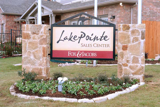 A sign with a parchment look mounted in a large iron frame with a pointed top and installed between two stone pillars
